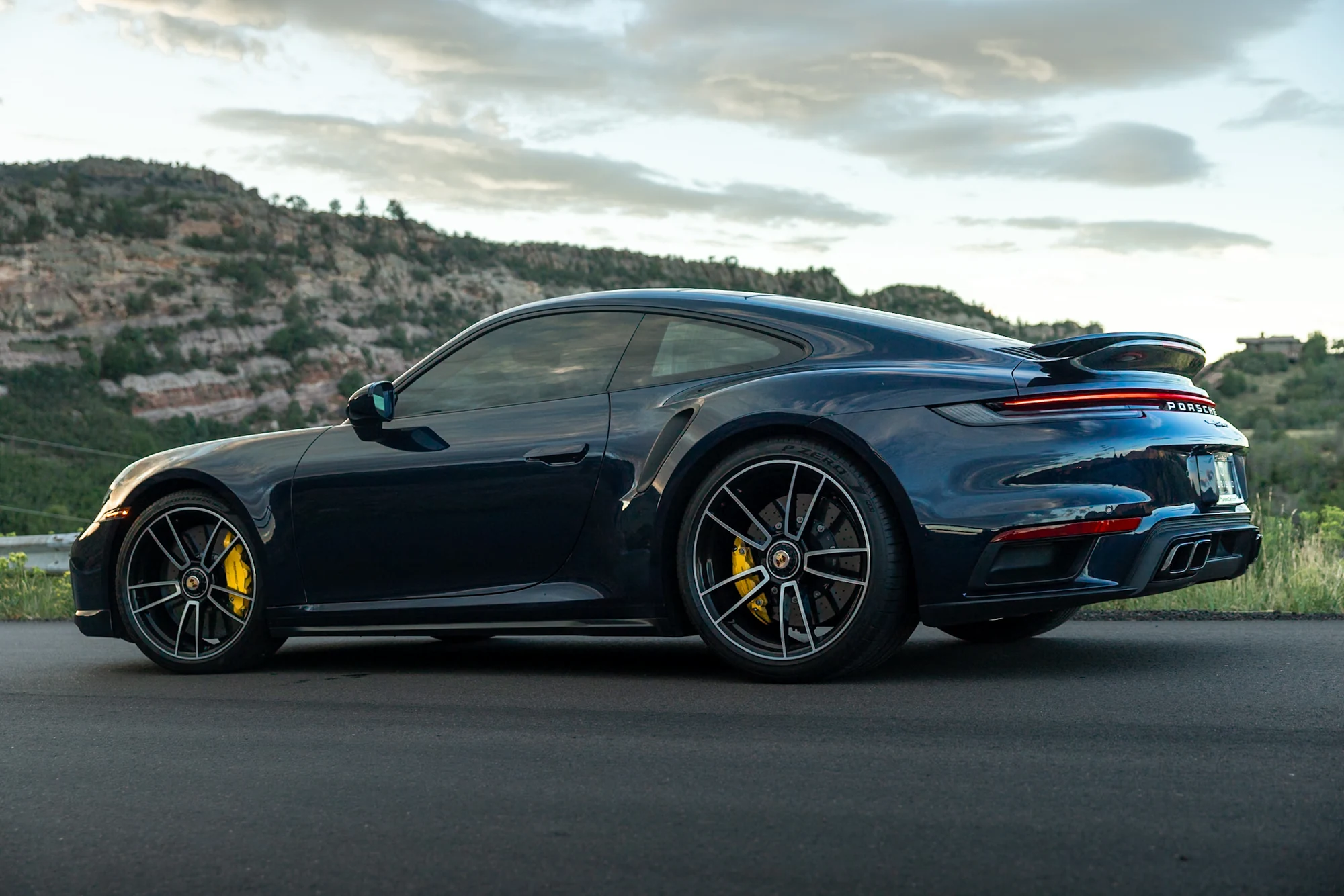 Dark blue Porsche 911 Turbo on a Colorado mountain road — luxury car consignment vs. private sale